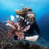 Diver wearing a khaki TUSA Zensee mask beside a lionfish