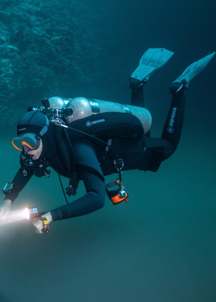 Sidemount diver swimming with two side cylinders and a dive light