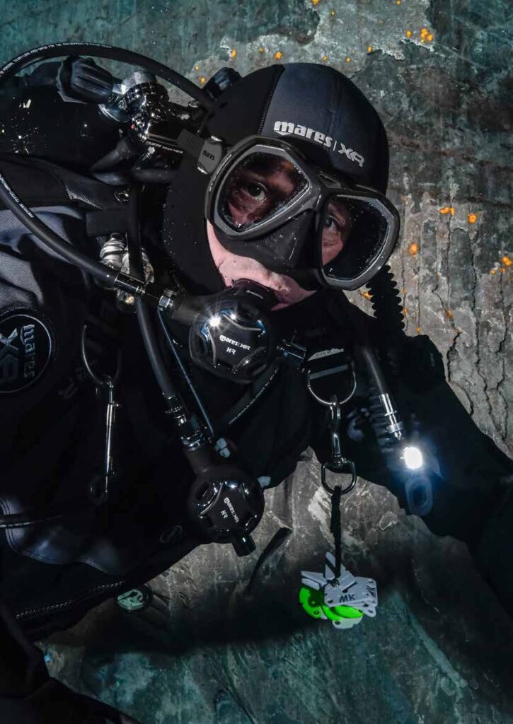 Technical diver with a compact dive light beside a cave wall