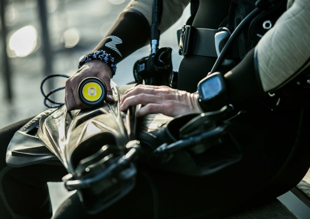 Hands checking a scuba cylinder valve and first stage on the shore