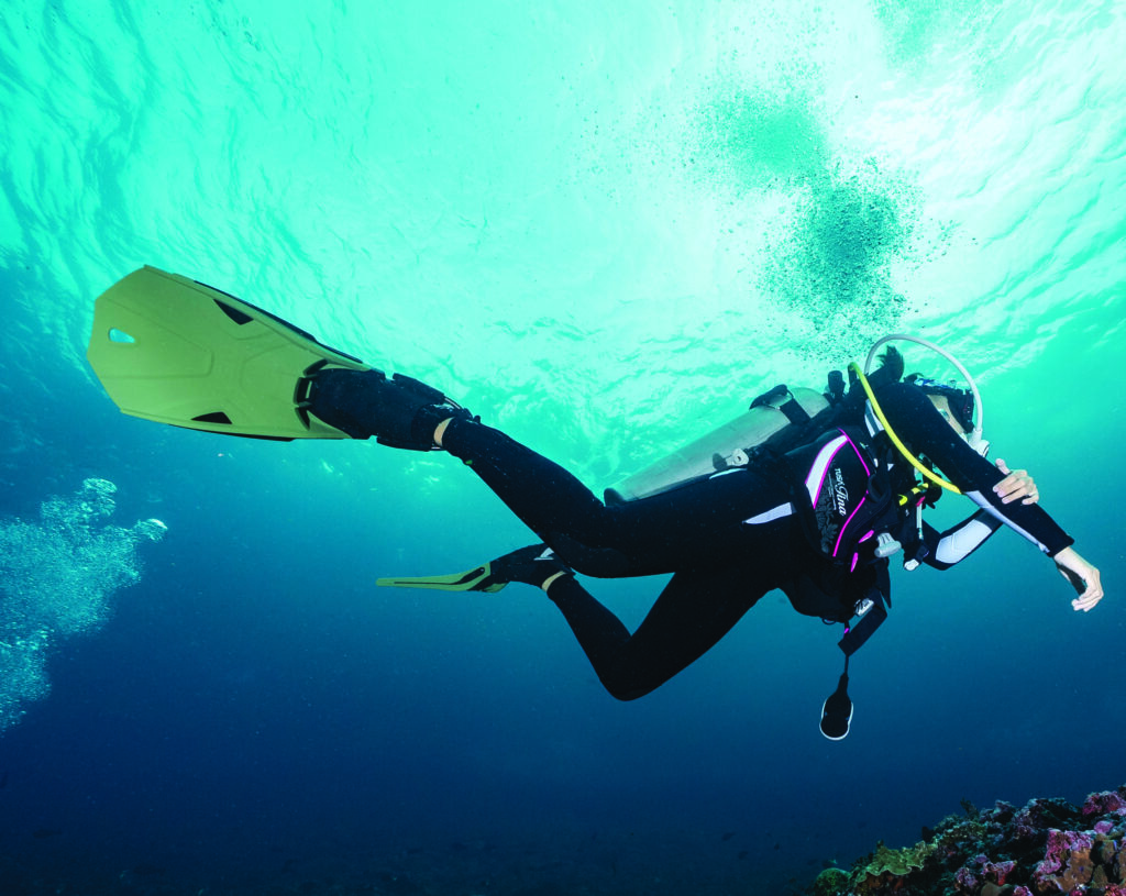 Scuba diver swimming through sunlit water with yellow fins